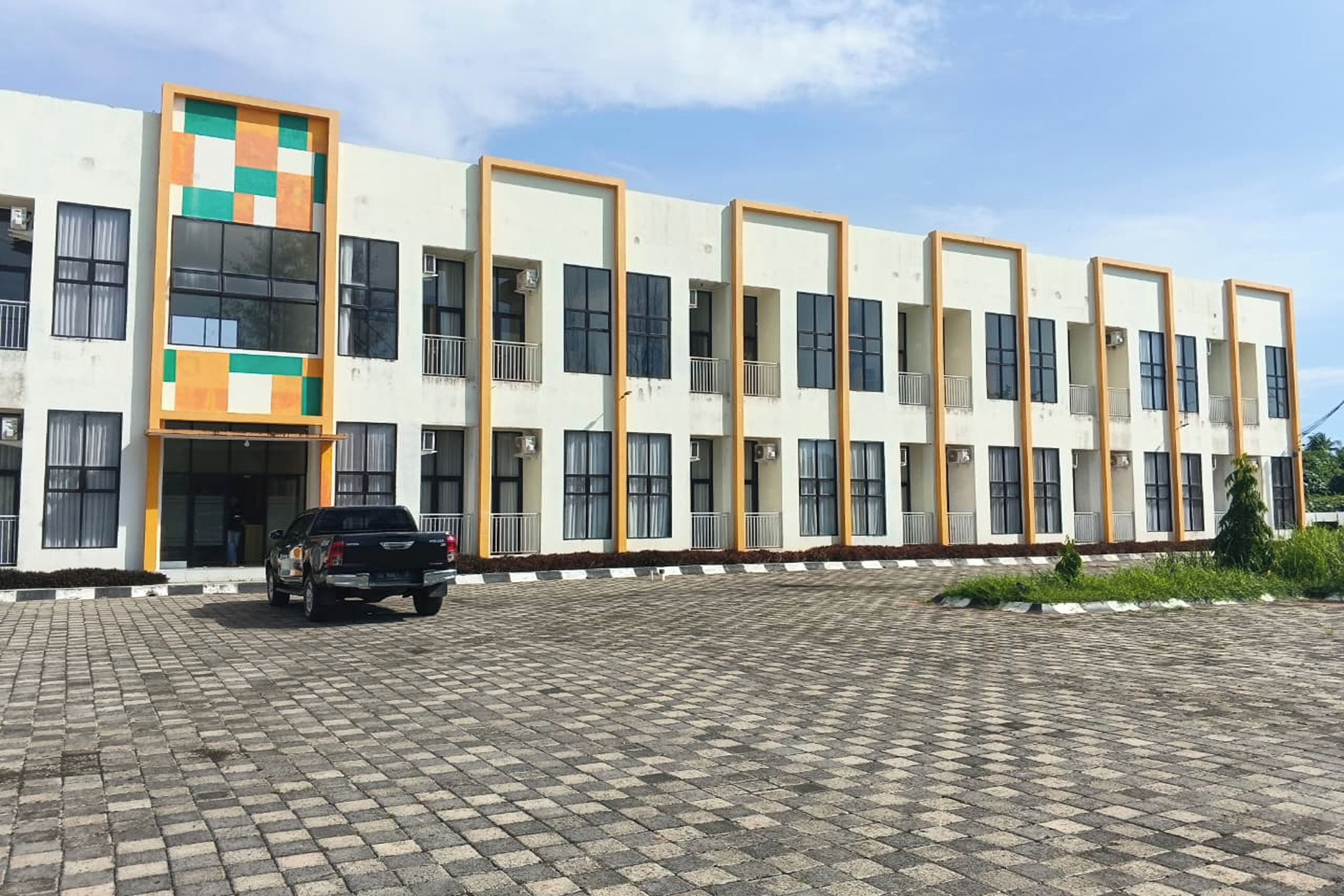 A multi-story building with a flat facade, large windows, and a parking area with a vehicle.