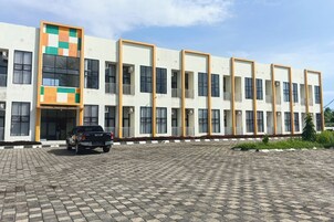 Un edificio de varios pisos con fachada plana, amplias ventanas y un estacionamiento con un vehículo.