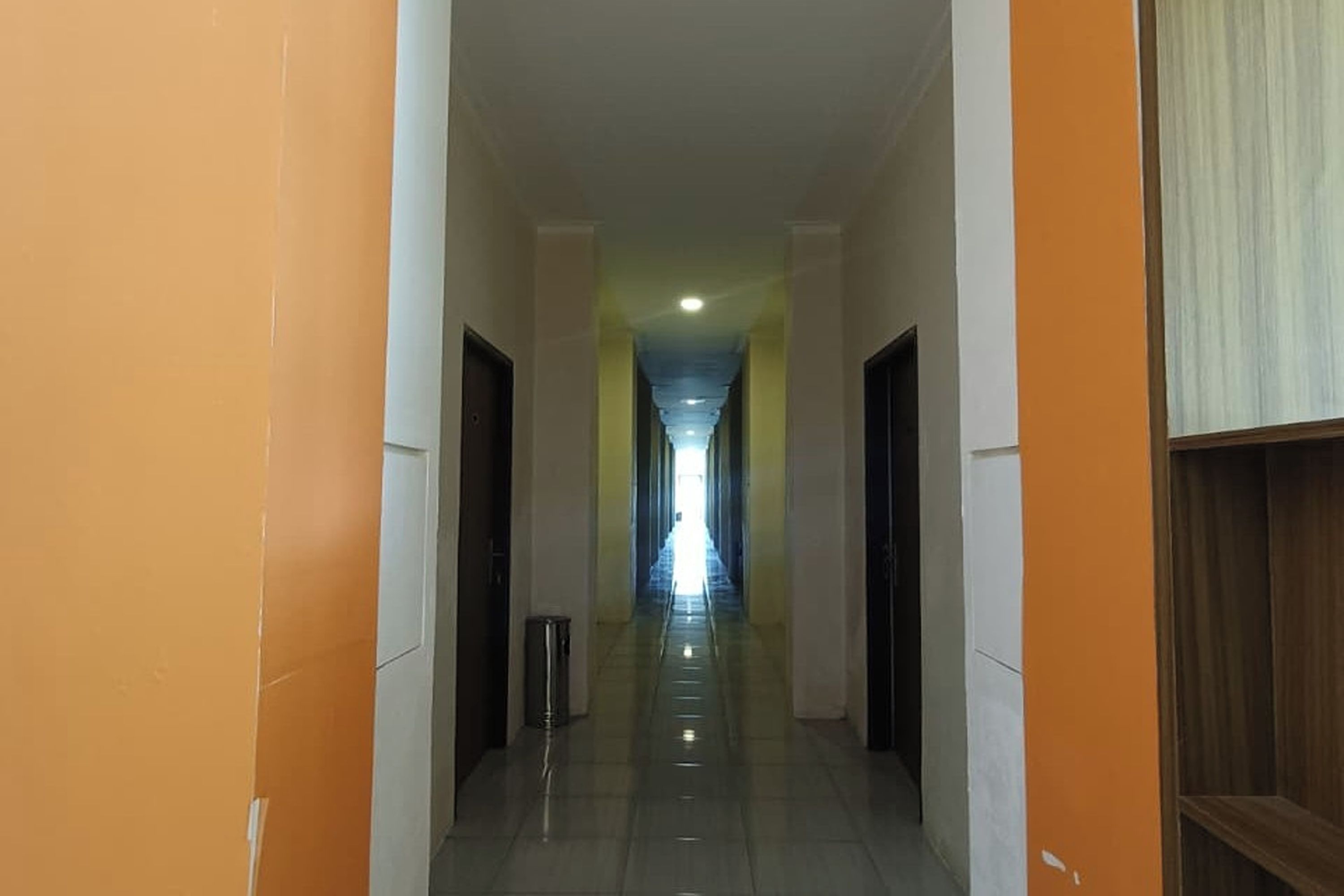 A corridor with doors on both sides, leading to a bright end.