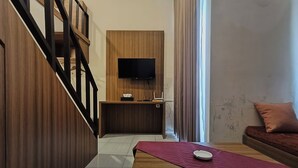 Una sala de estar moderna con piso de madera, un tapete rojo, un televisor de pantalla plana montado en una pared de madera, una mesita con un control remoto y un sofá marrón con un cojín.