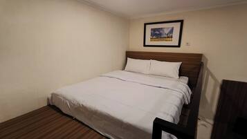 A single bed with a wooden headboard, a white bedspread, and a framed picture on the wall.