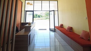 Un pasillo con mostrador de recepción, zona de estar con cojines y un amplio ventanal que da al exterior.