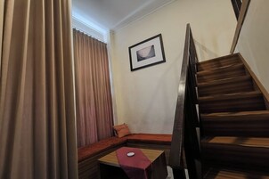 Una habitación de esquina con un banco de madera, una pequeña mesa, un cuadro enmarcado en la pared y una escalera.