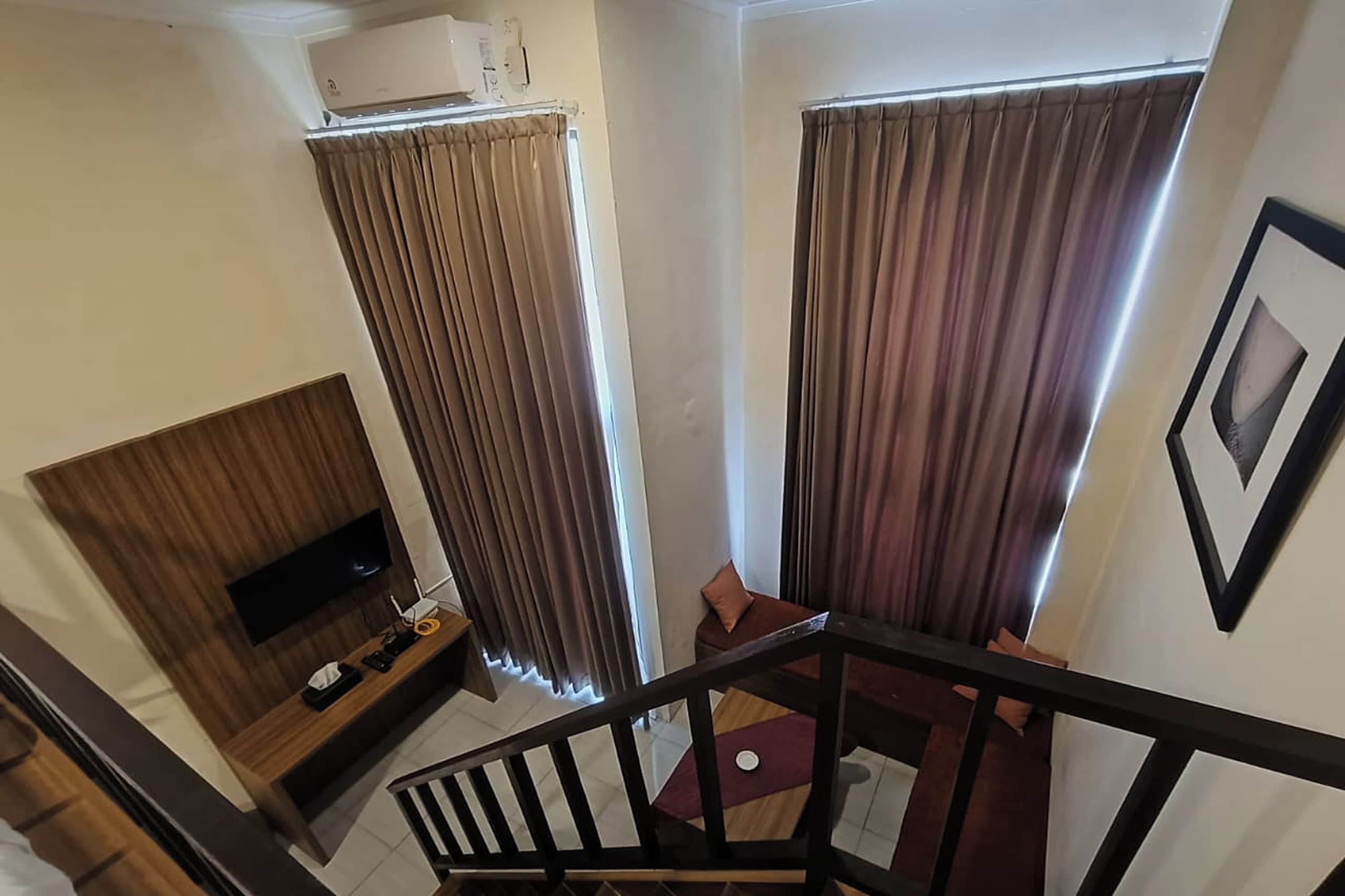 A hotel room with a bed, a TV, a desk, and a window with curtains.