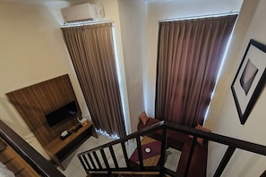 A hotel room with a bed, a TV, a desk, and a window with curtains.