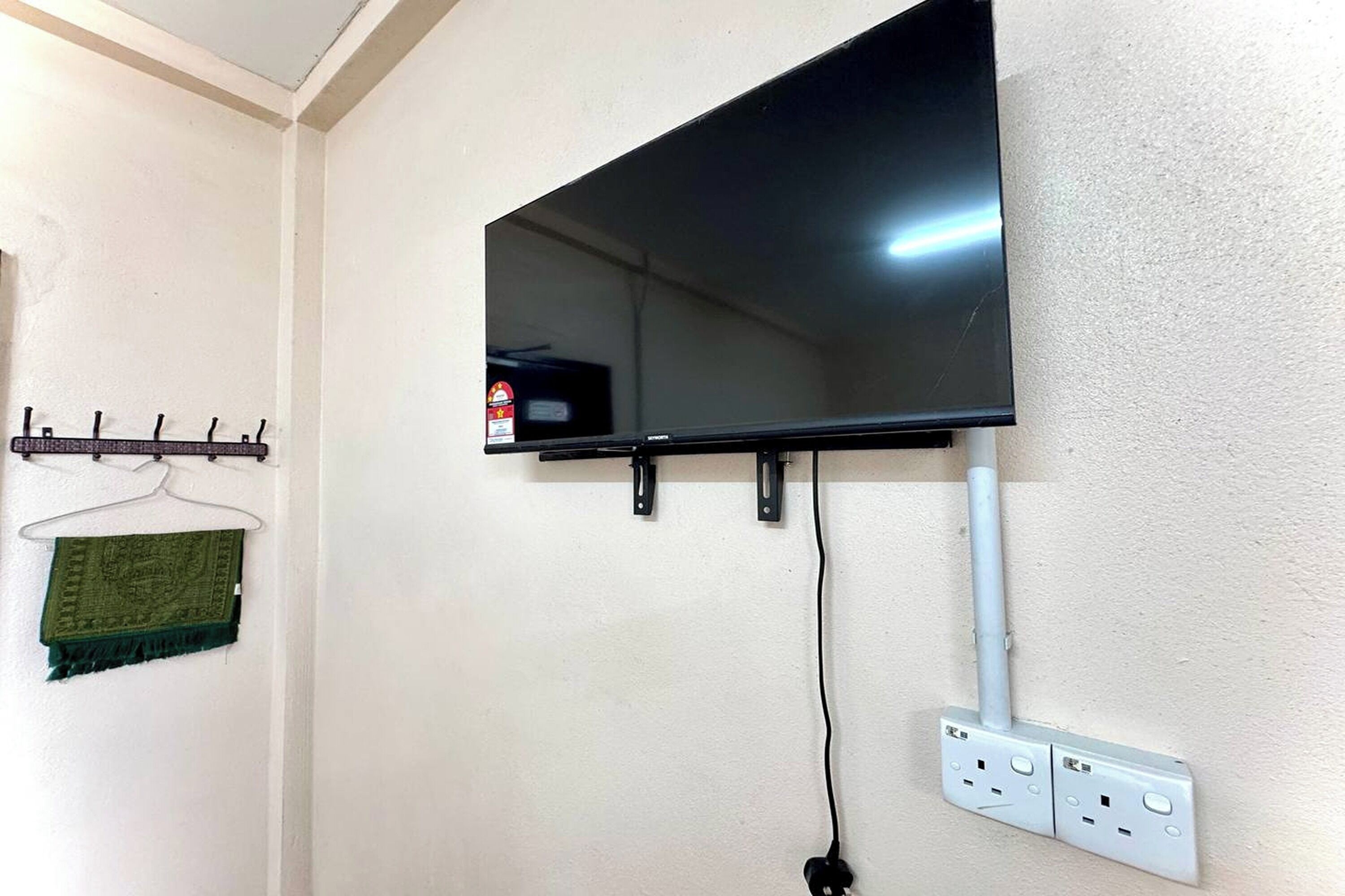 A wall-mounted TV, a power outlet, and a towel rack with a green towel.