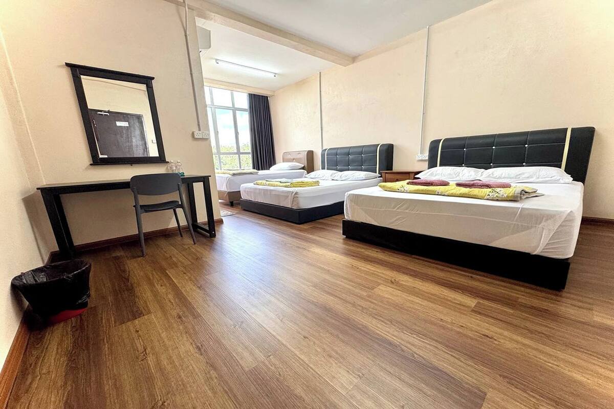 A hotel room with two beds, a desk, a chair, and a trash bin.