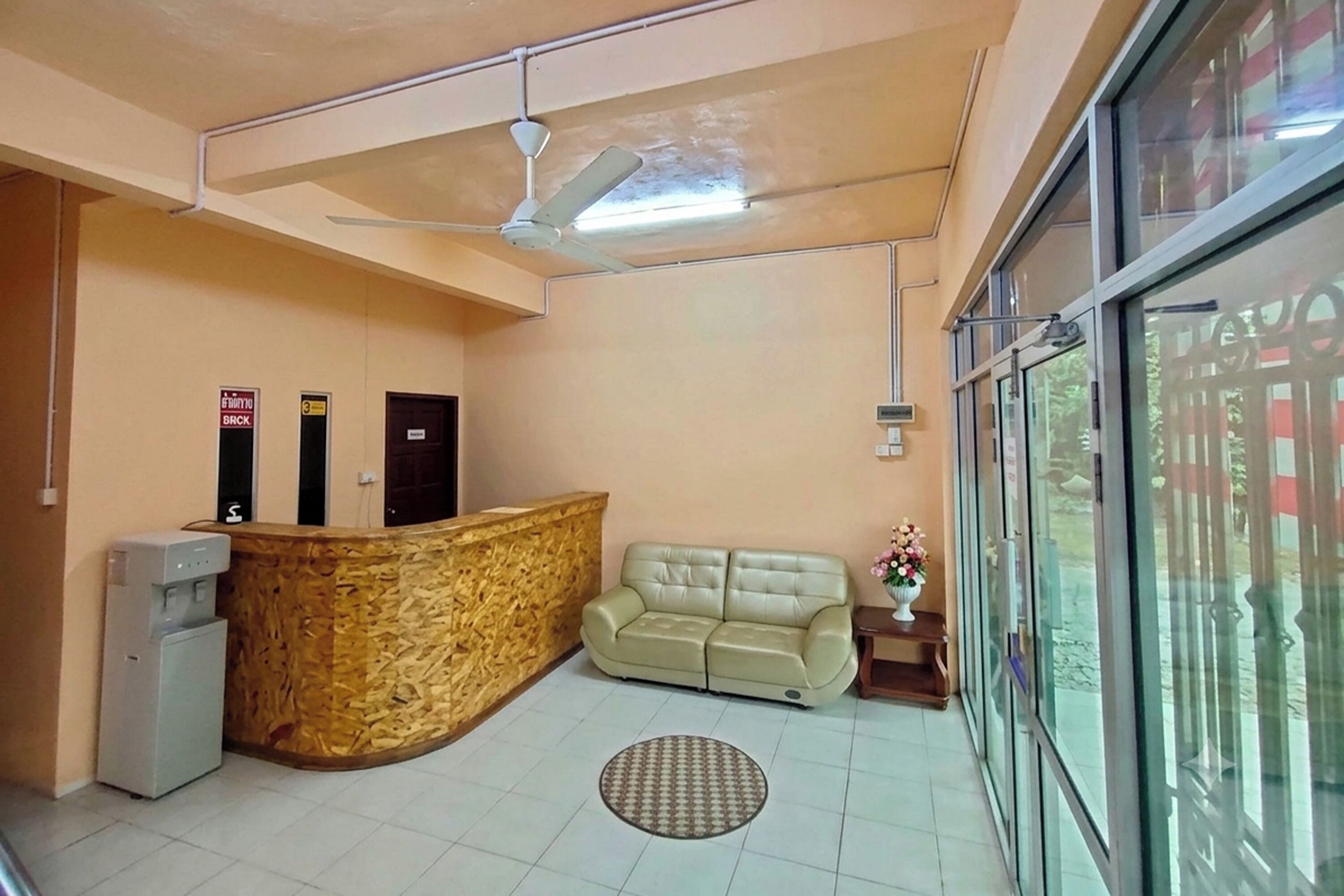 A reception area with a reception desk, a sofa, a water dispenser, a ceiling fan, and a large window.