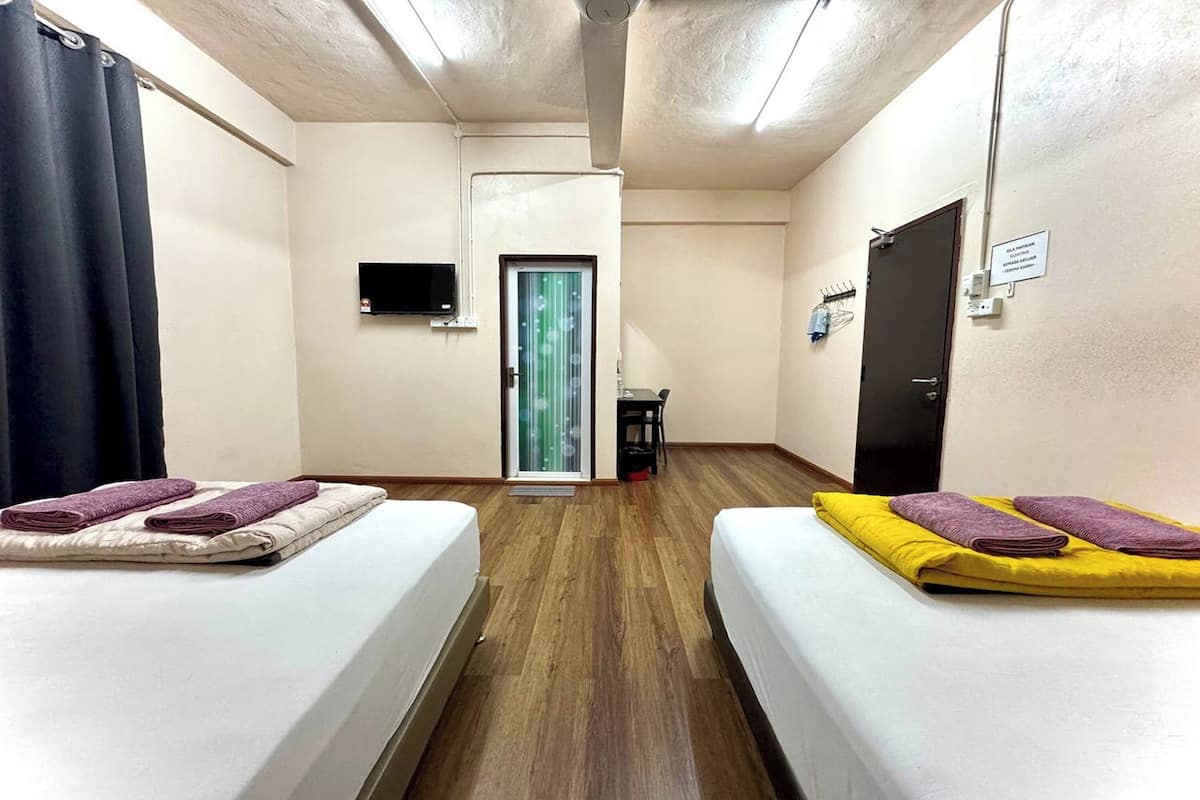 Habitación de hotel con dos camas, televisión, una puerta y una pequeña mesa.
