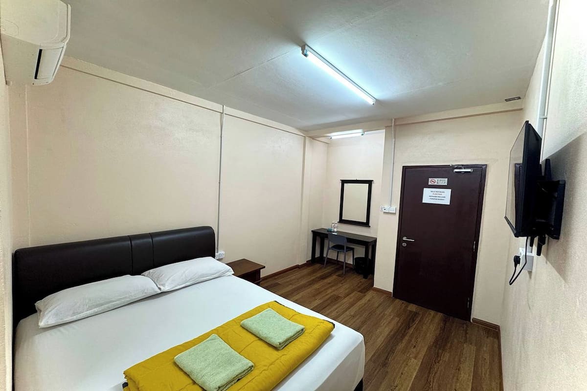 Habitación de hotel con cama, escritorio, silla, televisión y una puerta con un cartel.