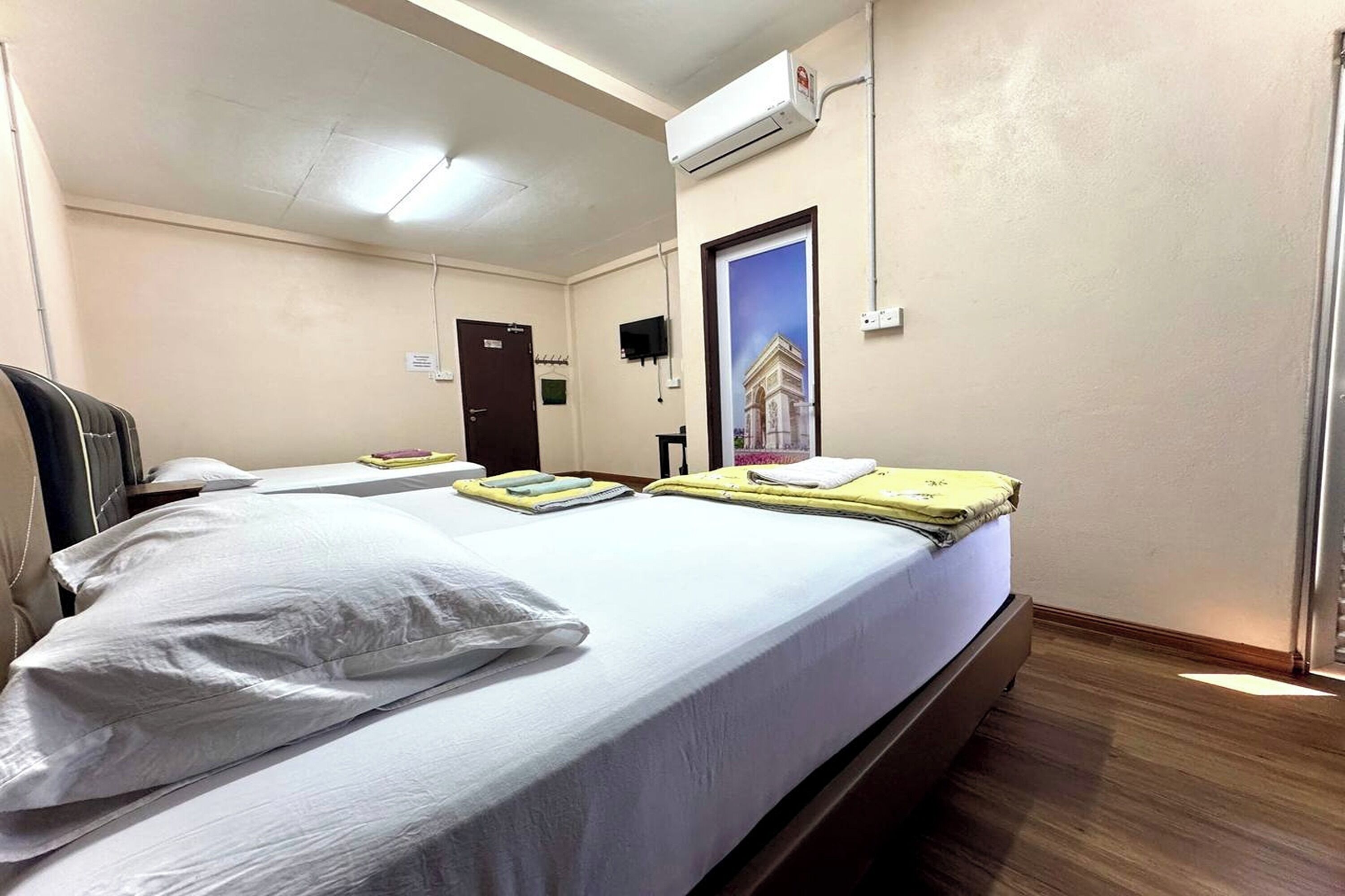 Ett hotellrum med en säng, ett skrivbord, en stol, en luftkonditioneringsanläggning, en dörr och en affisch på väggen.