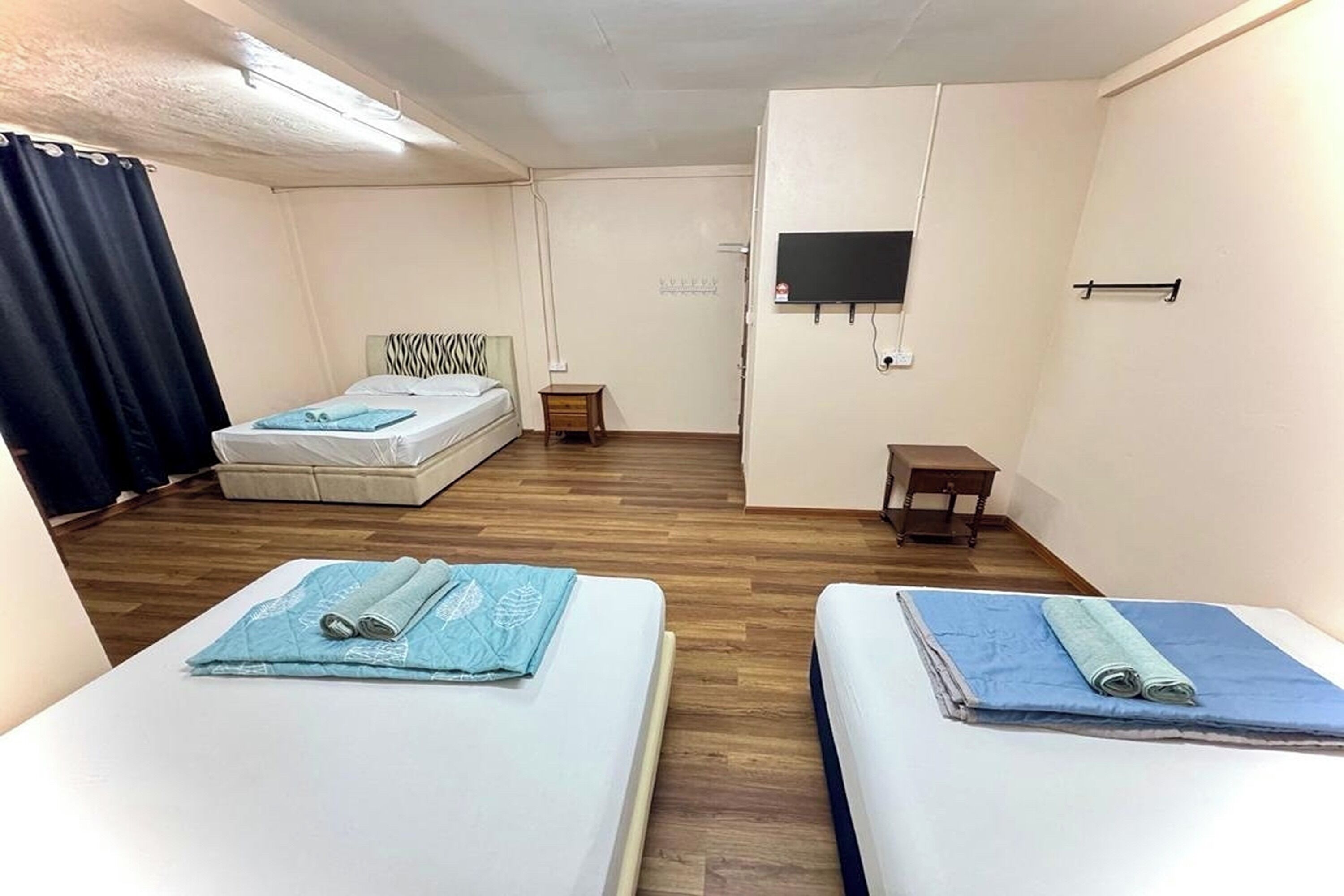 Een kamer met twee bedden, een aan de muur bevestigde televisie, een klein tafeltje en een raam met gordijnen.