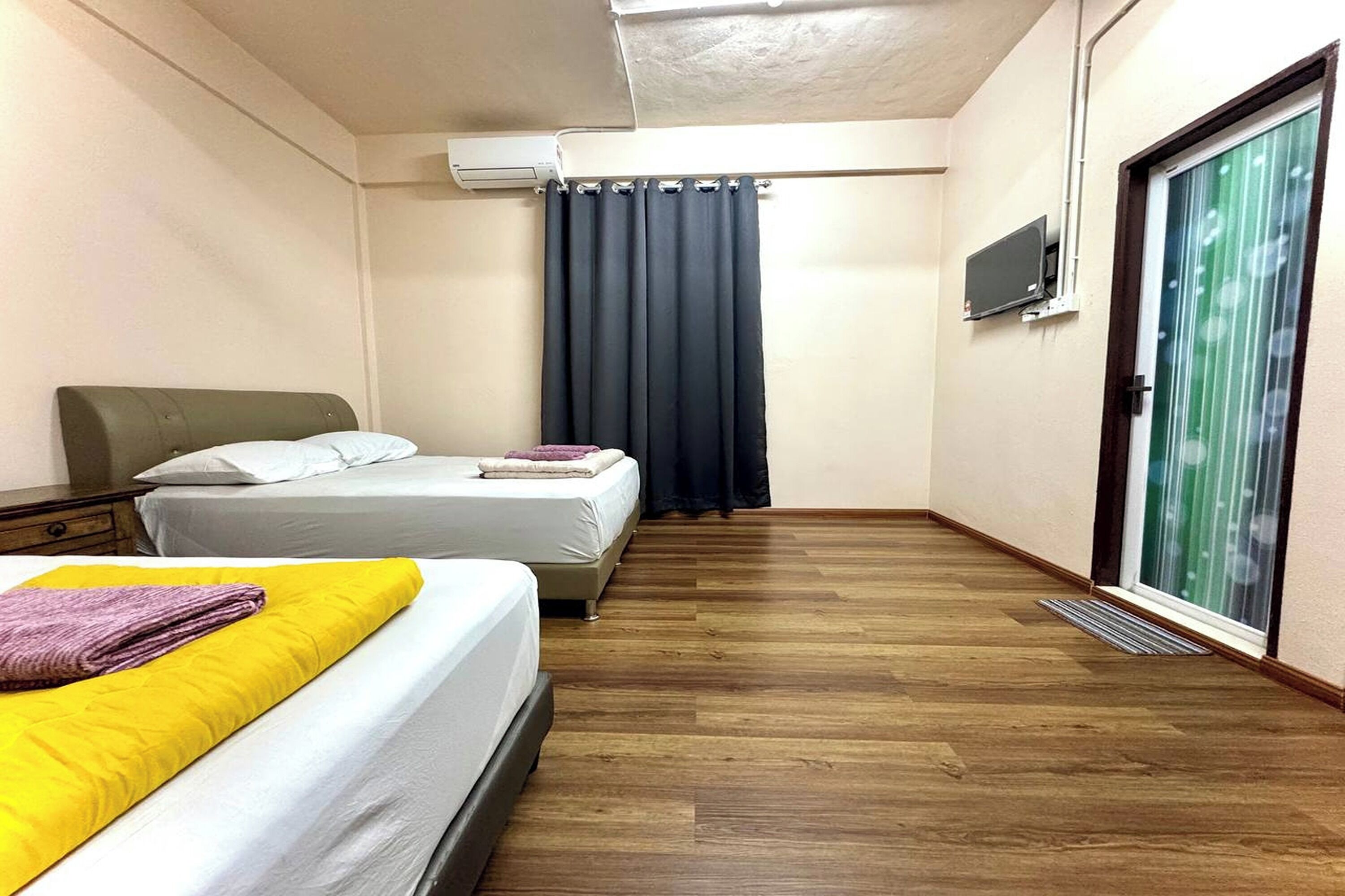 A hotel room with two beds, a flat-screen TV, a sliding glass door, and a ceiling air conditioner.