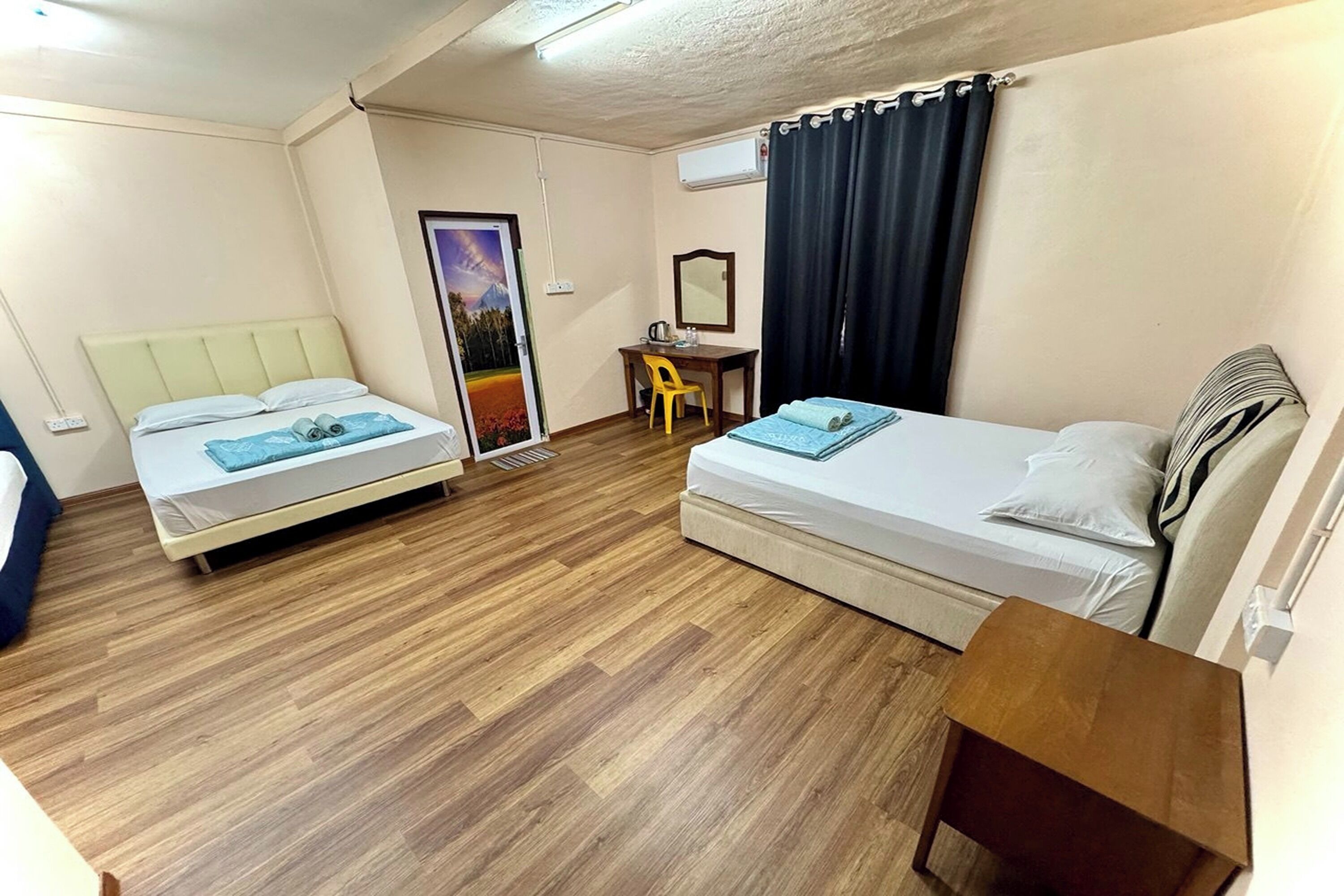 A room with two beds, a desk, a chair, a small table, and a window with curtains.
