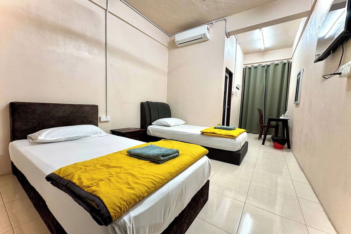 Habitación de hotel con dos camas, un escritorio, una silla, un equipo de aire acondicionado y una cortina.