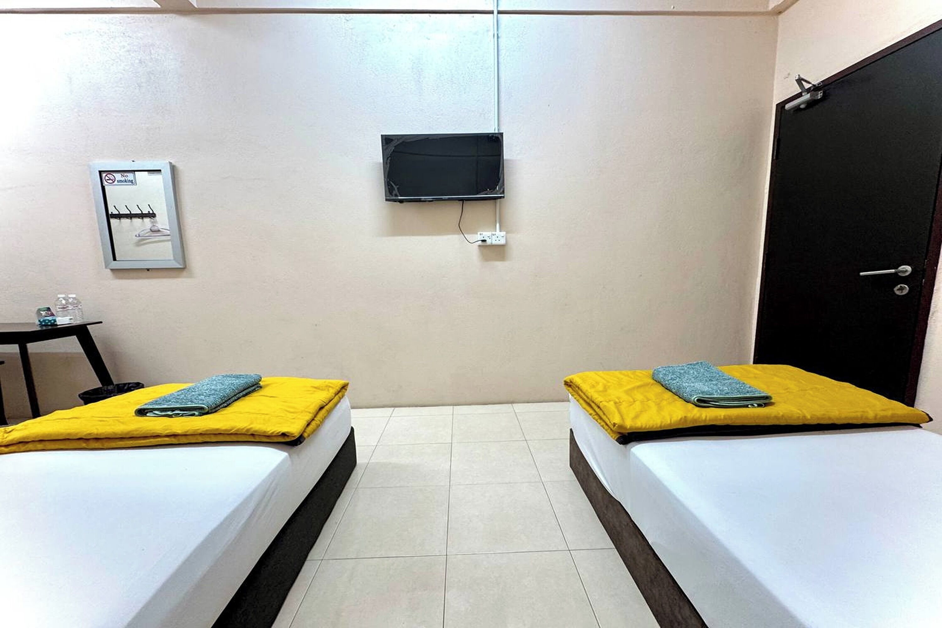 A room with two beds, a TV mounted on the wall, a door, and a small table with a chair.