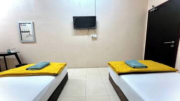 A room with two beds, a TV mounted on the wall, a door, and a small table with a chair.