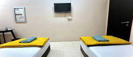 A room with two beds, a TV mounted on the wall, a door, and a small table with a chair.