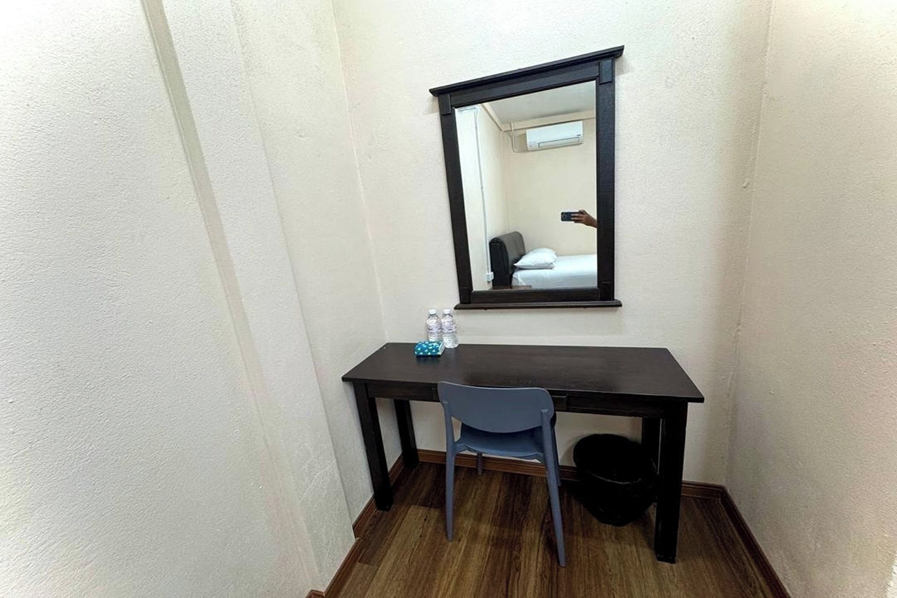 A small room with a dark wooden desk, a chair, a mirror, and a small trash bin.