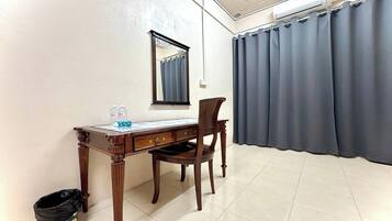 Una habitación con un escritorio de madera, una silla, un espejo, un ventanal con cortinas y un cesto de basura.
