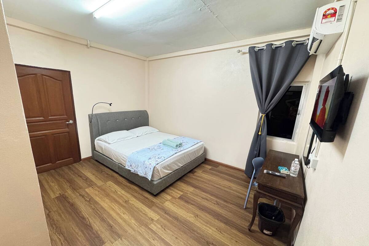 A small, neatly arranged room with a bed, a desk, a chair, a TV, and an air conditioning unit.