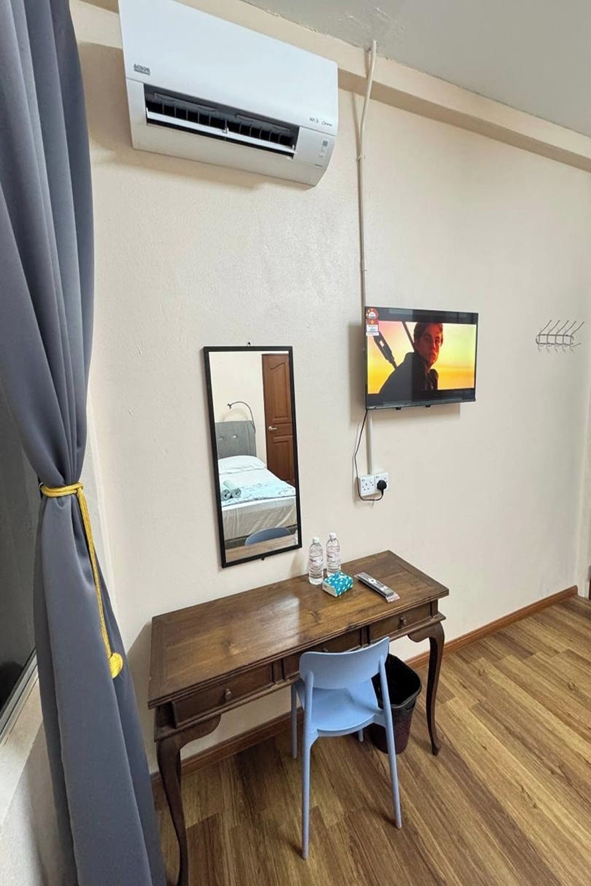Habitación de hotel con un escritorio de madera, una silla, televisor, aire acondicionado y un espejo.