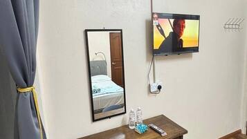 Habitación de hotel con un escritorio de madera, una silla, televisor, aire acondicionado y un espejo.
