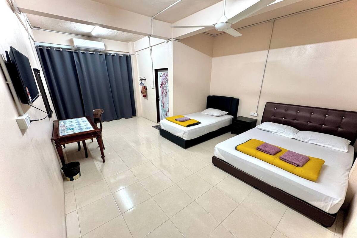 A hotel room with two beds, a desk, a chair, and a ceiling fan.