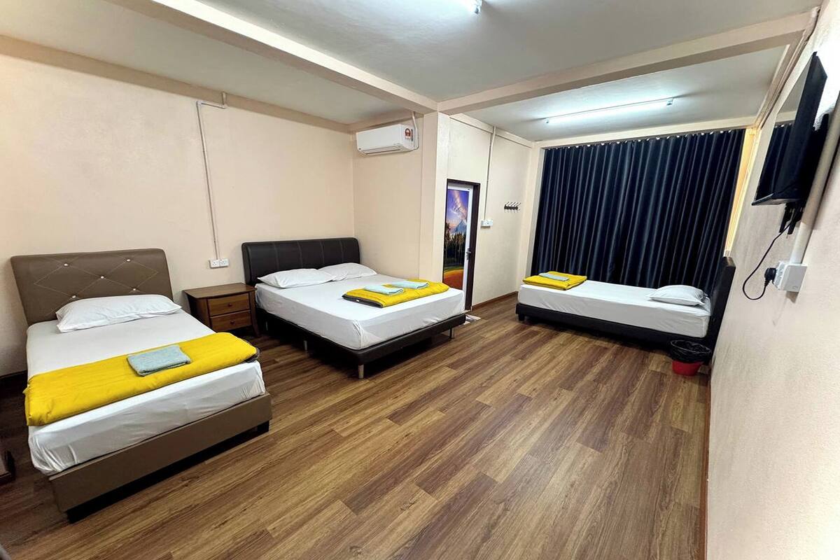 A hotel room with three beds, a flat-screen TV, an air conditioning unit, and a wooden floor.