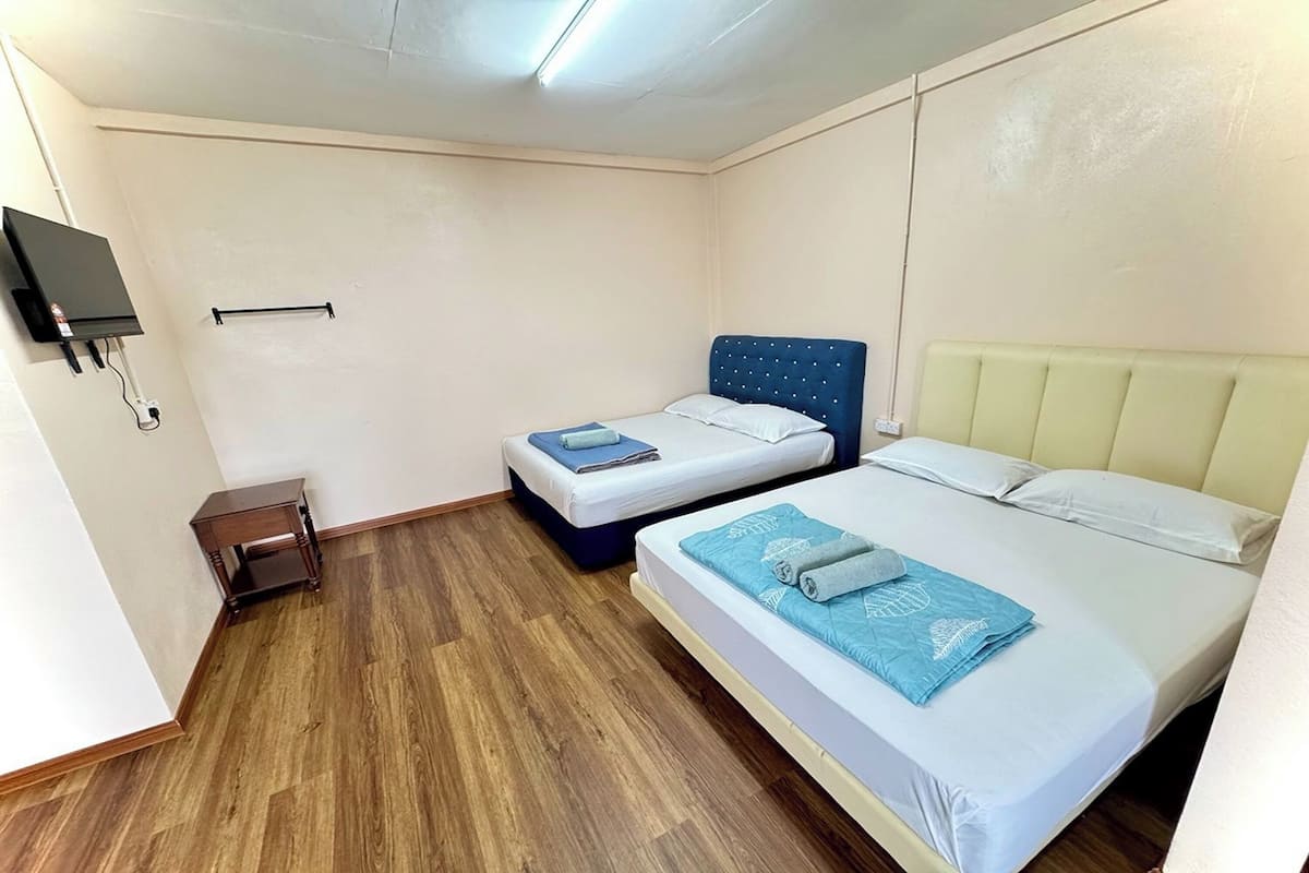 Una habitación con dos camas, una mesita pequeña, un televisor montado en la pared y suelo de madera.
