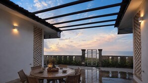 Un patio al aire libre con una mesa y sillas de madera redonda, una pérgola y vistas al mar.