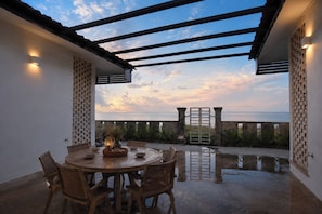 Une terrasse extérieure avec une table et des chaises en bois rondes, une pergola et une vue sur la mer.