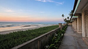 Vista costera con un camino de hormigón, palmeras y una playa.