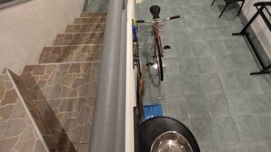 A staircase with a bicycle leaning against it, a trash bin, and a small table with chairs. - Terminal Garage (Phuket)