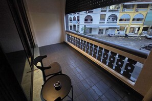 A balcony with a chair and a table, a railing, and a view of a building with multiple stories and balconies. - Terminal Garage (Phuket)