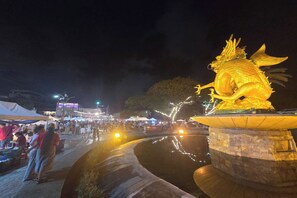 A nighttime outdoor setting with a golden dragon statue on a stone pedestal, surrounded by a body of water reflecting lights. - Terminal Garage (Phuket)