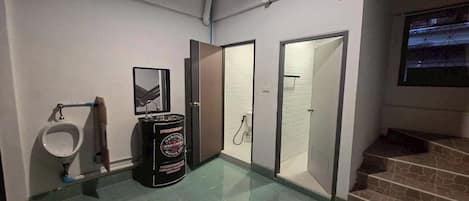 Baño de hombres con orinal, bote de basura, puerta y una escalera que sube a un nivel superior.