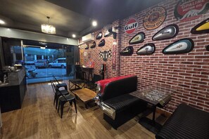 A restaurant interior with a brick wall, vintage car decals, a black leather couch, and a wooden table. - Terminal Garage (Phuket)