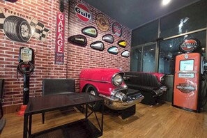 A vintage-themed room with a red car, a Harley-Davidson gas pump, and a wall adorned with automotive memorabilia. - Terminal Garage (Phuket)