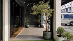 A modern building entrance with artificial grass, potted plants, and a vehicle parked outside. - Terminal Garage (Phuket)