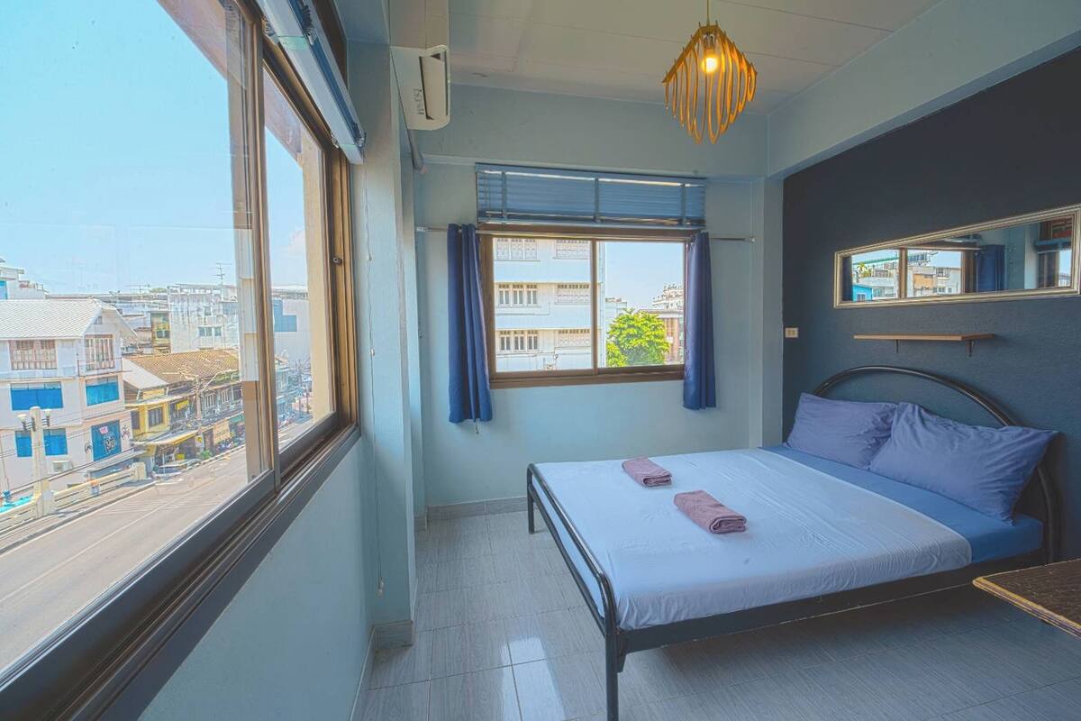 Un dormitorio con cama, ventana, espejo y lámpara colgante.