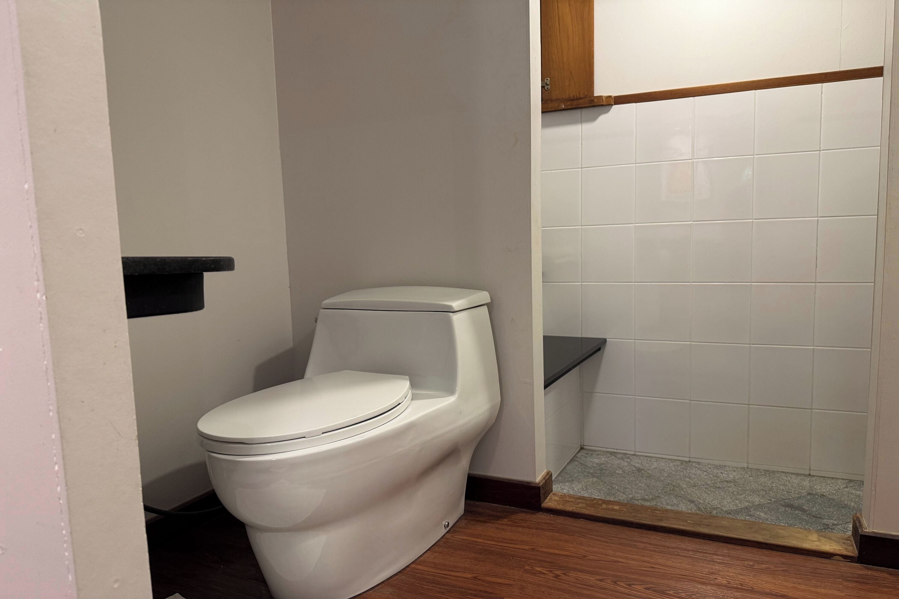 A white toilet, a wooden floor, and a tiled wall in a bathroom.