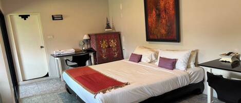 A hotel room with a bed, desk, chair, and a decorative cabinet.