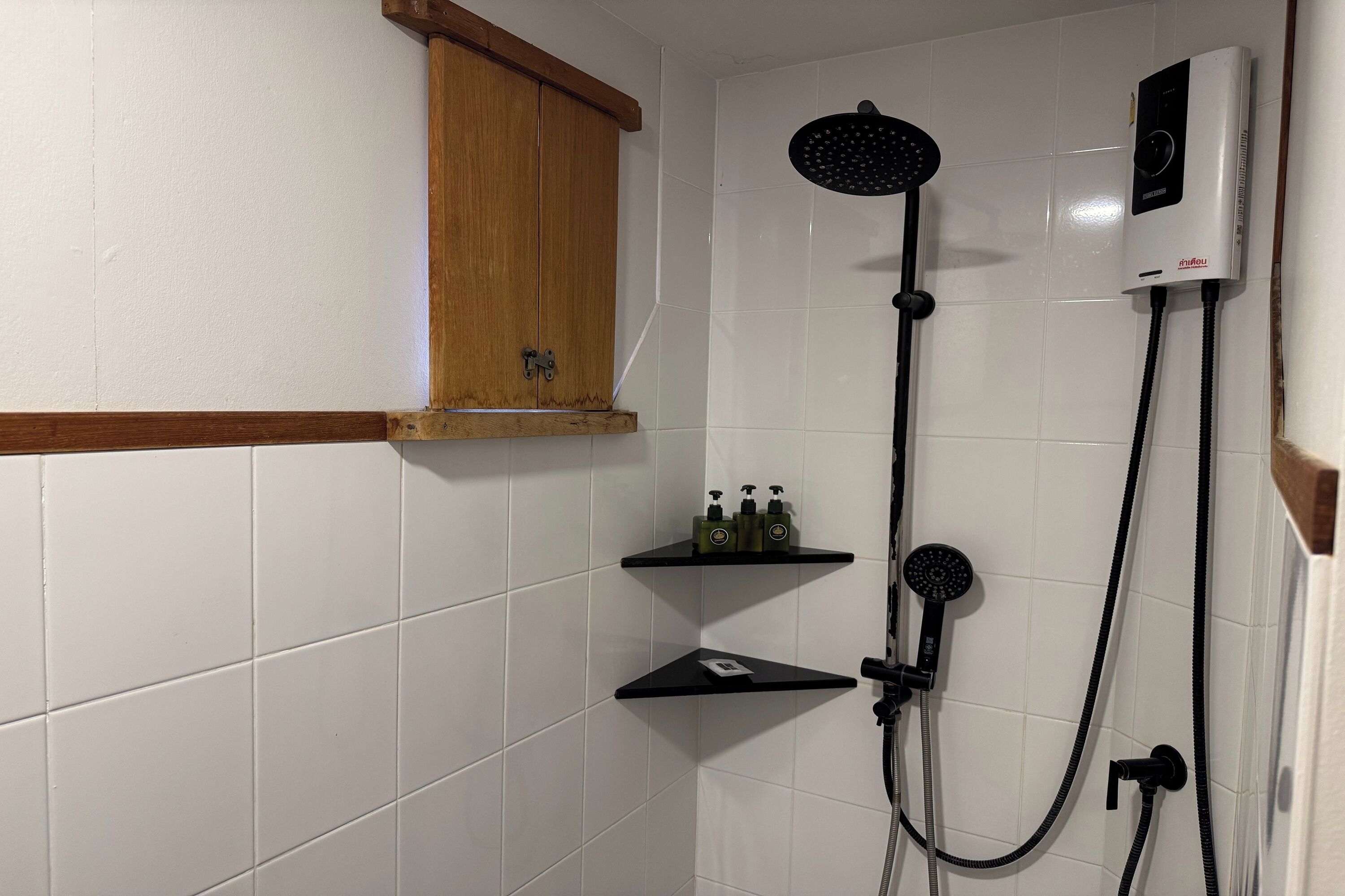 A shower with a handheld showerhead and a wall-mounted control panel. There are two black shelves with toiletries.