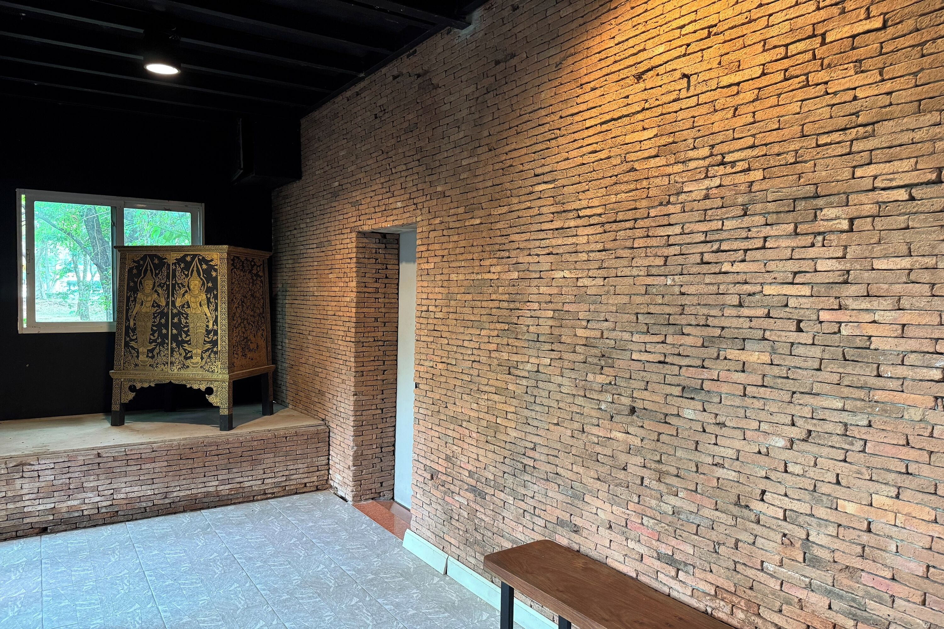 A room with a brick wall, a bench, and a cabinet with intricate designs.