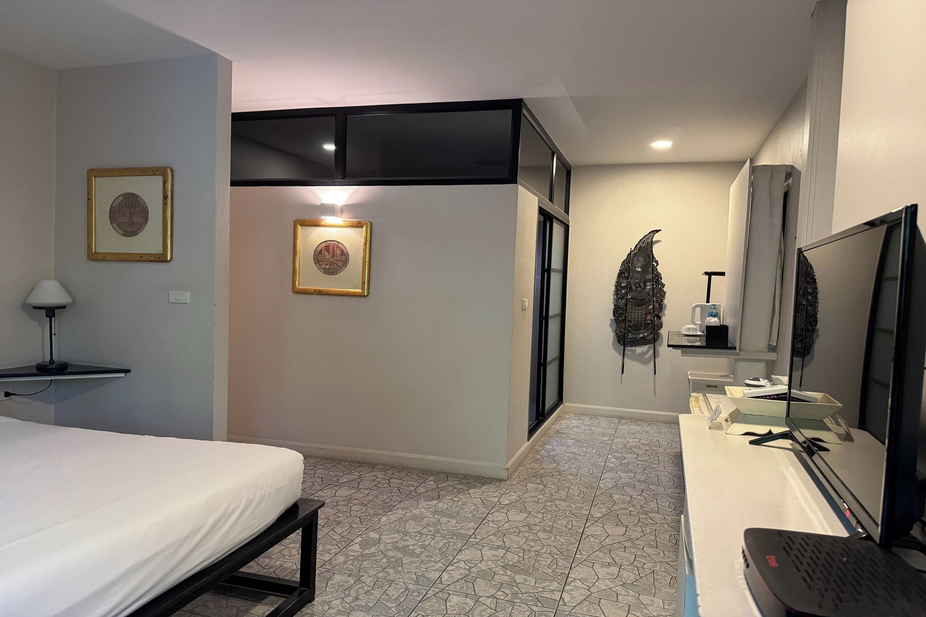 A hotel room with a bed, a desk with a computer, a TV, and framed pictures on the wall.