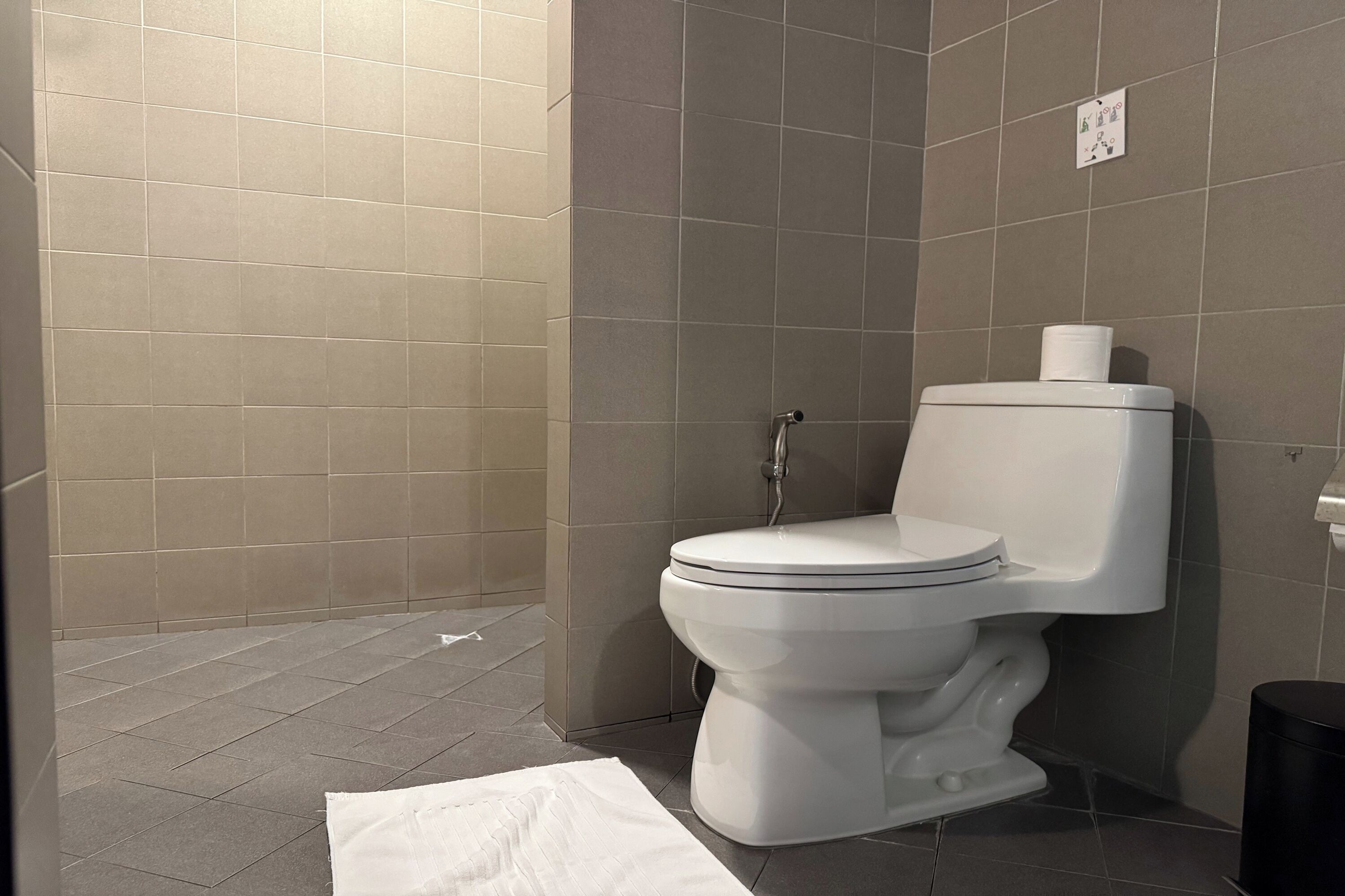 A bathroom with a toilet, a shower area, and a trash bin.