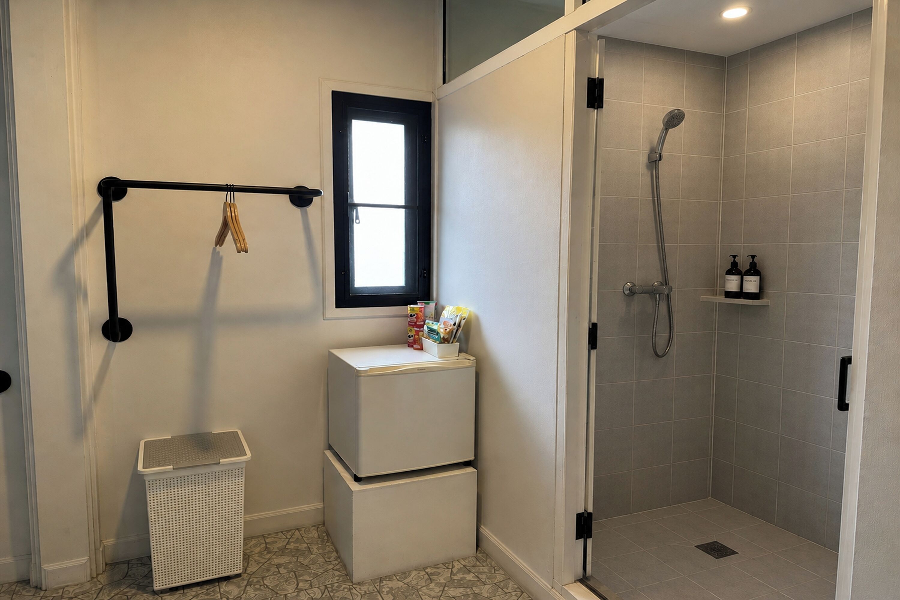 A bathroom with a shower, a toilet, a laundry basket, and a window.