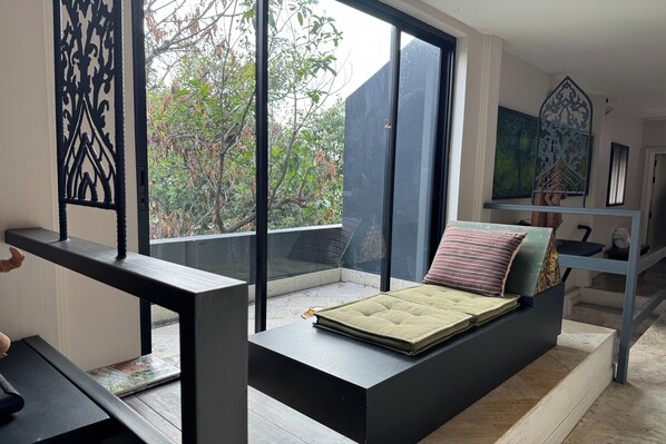 A modern room with a large window, a bed with pillows, a desk, and a staircase.