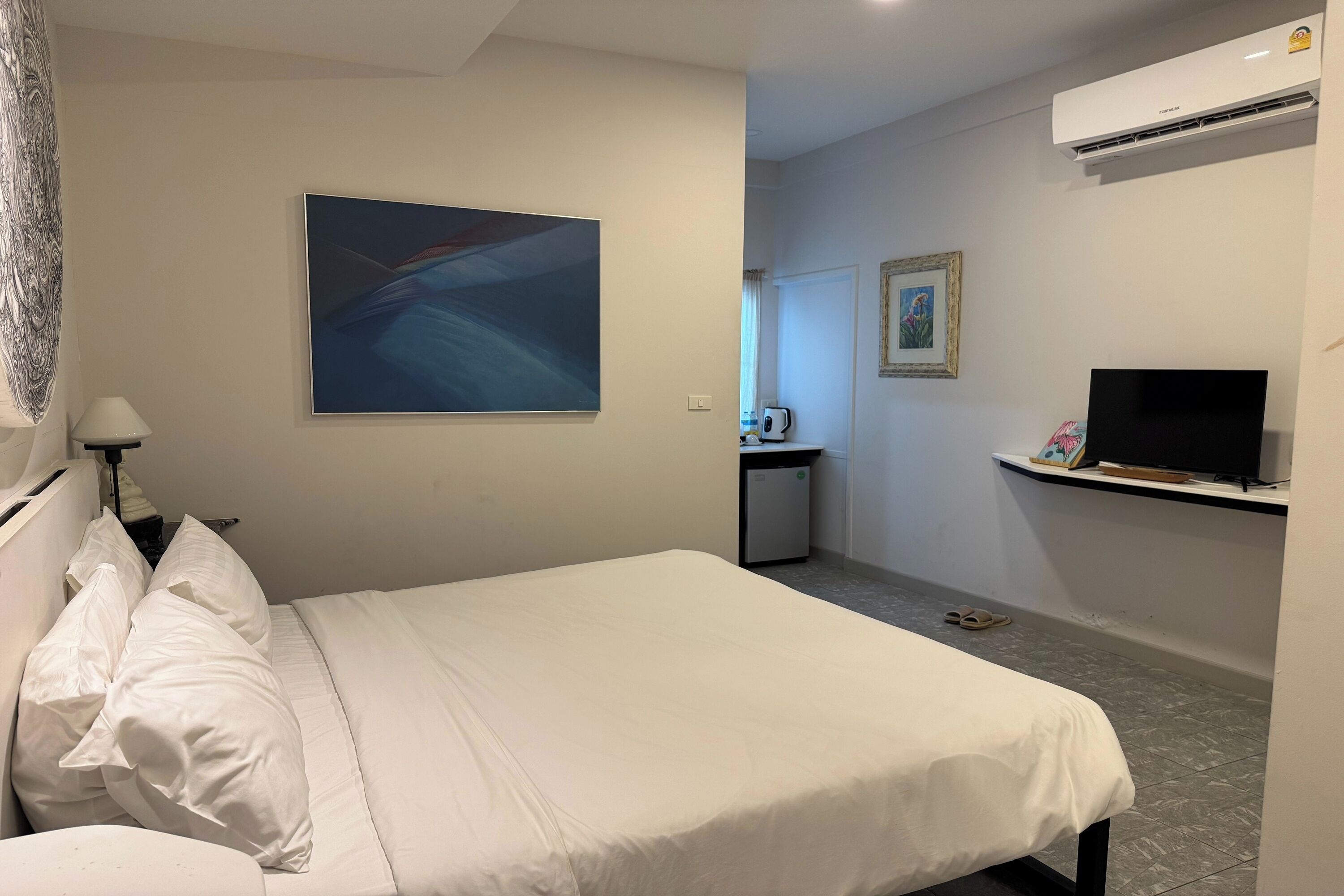 A hotel room with a bed, a television, an air conditioner, and a painting on the wall.